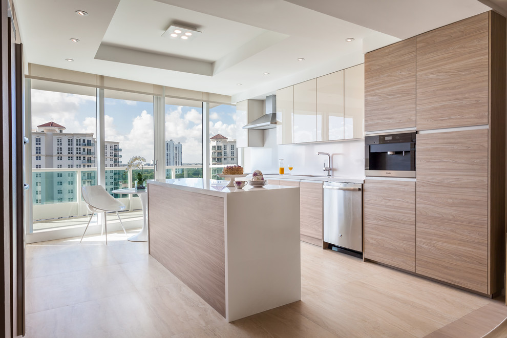 Diseño de cocina comedor contemporánea con armarios con paneles lisos, puertas de armario de madera clara, salpicadero blanco, electrodomésticos de acero inoxidable y una isla
