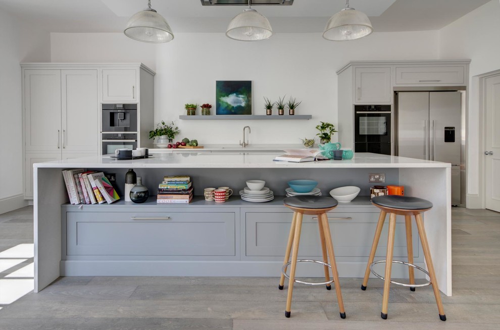 Photo of a large contemporary single-wall open plan kitchen in London with recessed-panel cabinets, grey cabinets, quartz worktops, stainless steel appliances, medium hardwood flooring, an island, beige floors and white worktops.