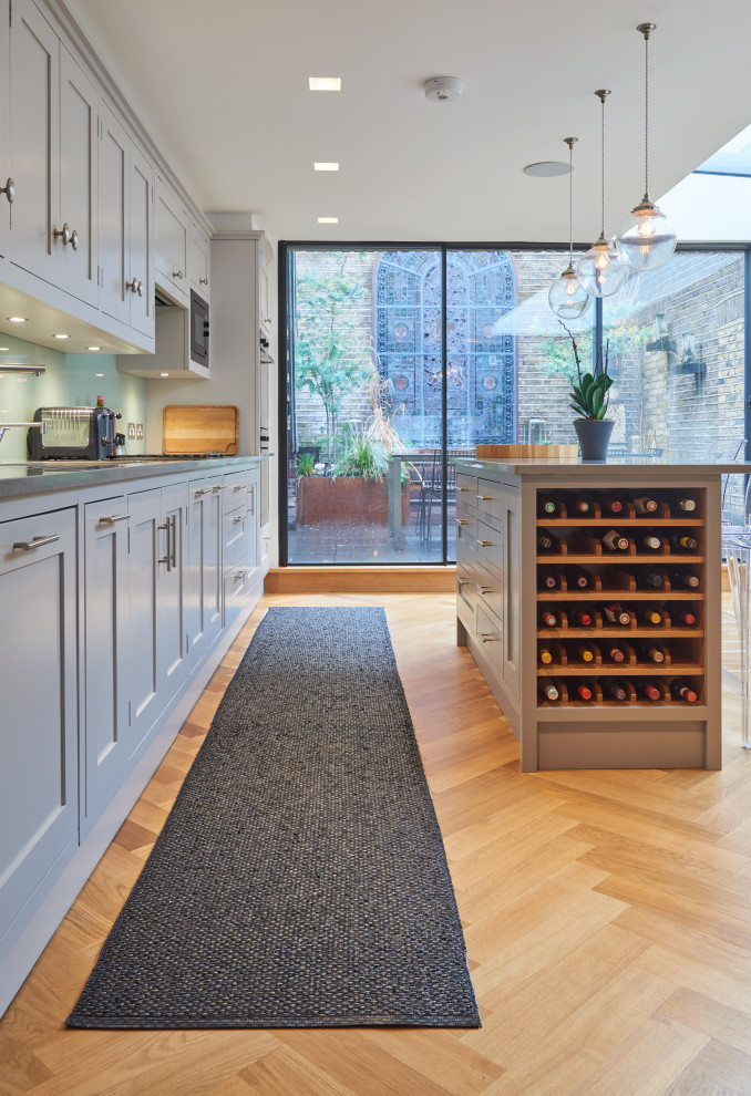 ロンドンにある高級な中くらいなトランジショナルスタイルのおしゃれなキッチン (アンダーカウンターシンク、シェーカースタイル扉のキャビネット、グレーのキャビネット、人工大理石カウンター、緑のキッチンパネル、ガラス板のキッチンパネル、シルバーの調理設備、淡色無垢フローリング、茶色い床、グレーのキッチンカウンター) の写真