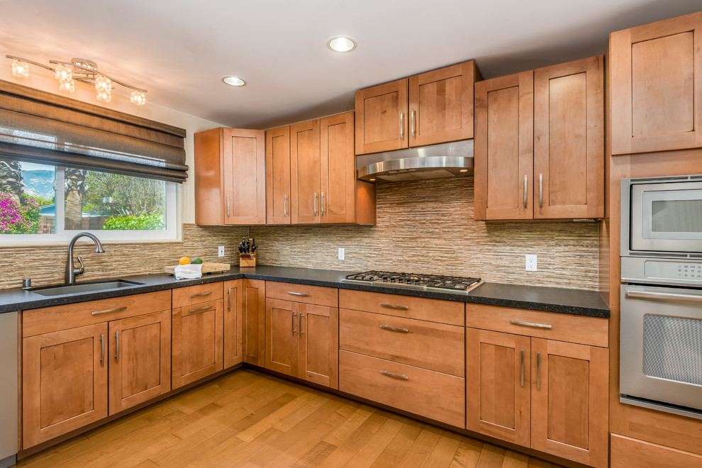 Example of a large transitional u-shaped medium tone wood floor and brown floor open concept kitchen design in Santa Barbara with an integrated sink, shaker cabinets, medium tone wood cabinets, quartz countertops, multicolored backsplash, porcelain backsplash, stainless steel appliances, no island and black countertops