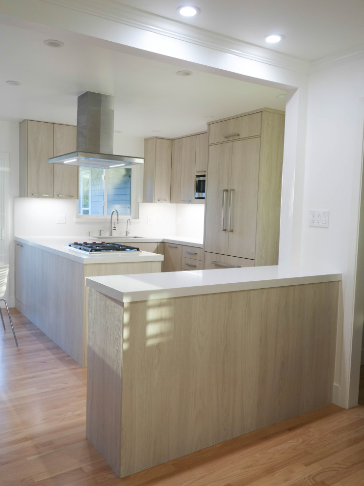 Bild på ett mellanstort funkis vit vitt kök, med en undermonterad diskho, släta luckor, skåp i ljust trä, bänkskiva i kvarts, vitt stänkskydd, stänkskydd i sten, integrerade vitvaror, ljust trägolv, en köksö och beiget golv