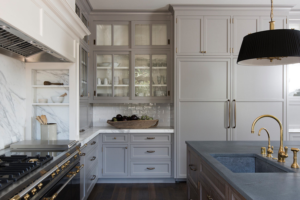 Inredning av ett klassiskt grå grått l-kök, med en undermonterad diskho, luckor med infälld panel, grå skåp, vitt stänkskydd, stänkskydd i sten, mörkt trägolv, en köksö och brunt golv
