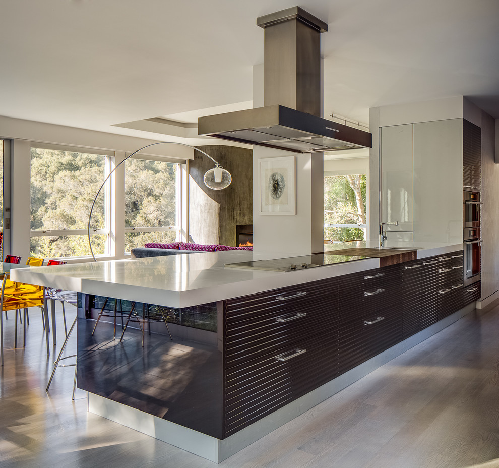 This is an example of a large modern galley open plan kitchen in San Francisco with a submerged sink, flat-panel cabinets, grey cabinets, composite countertops, blue splashback, glass sheet splashback, stainless steel appliances and a breakfast bar.