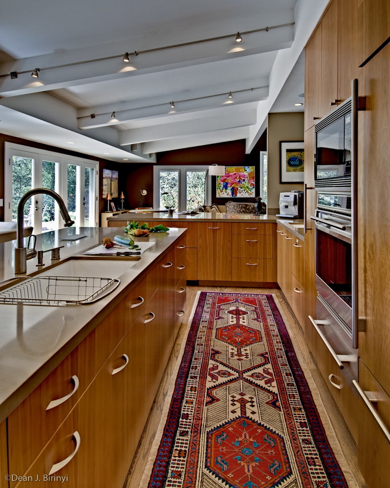 Example of a large eclectic galley light wood floor eat-in kitchen design in San Francisco with an undermount sink, solid surface countertops, stainless steel appliances, a peninsula, flat-panel cabinets and medium tone wood cabinets