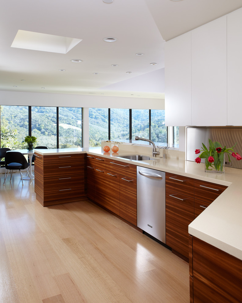 Inspiration for a mid-sized modern u-shaped medium tone wood floor and brown floor eat-in kitchen remodel in San Francisco with an undermount sink, flat-panel cabinets, medium tone wood cabinets, solid surface countertops, white backsplash, stone slab backsplash, stainless steel appliances and an island