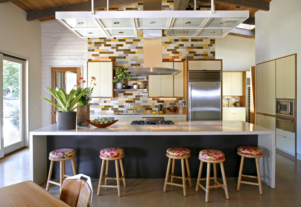 Cette image montre une cuisine parallèle design avec un électroménager en acier inoxydable, un placard à porte plane, des portes de placard beiges, un plan de travail en terrazzo, une crédence multicolore et une crédence en céramique.