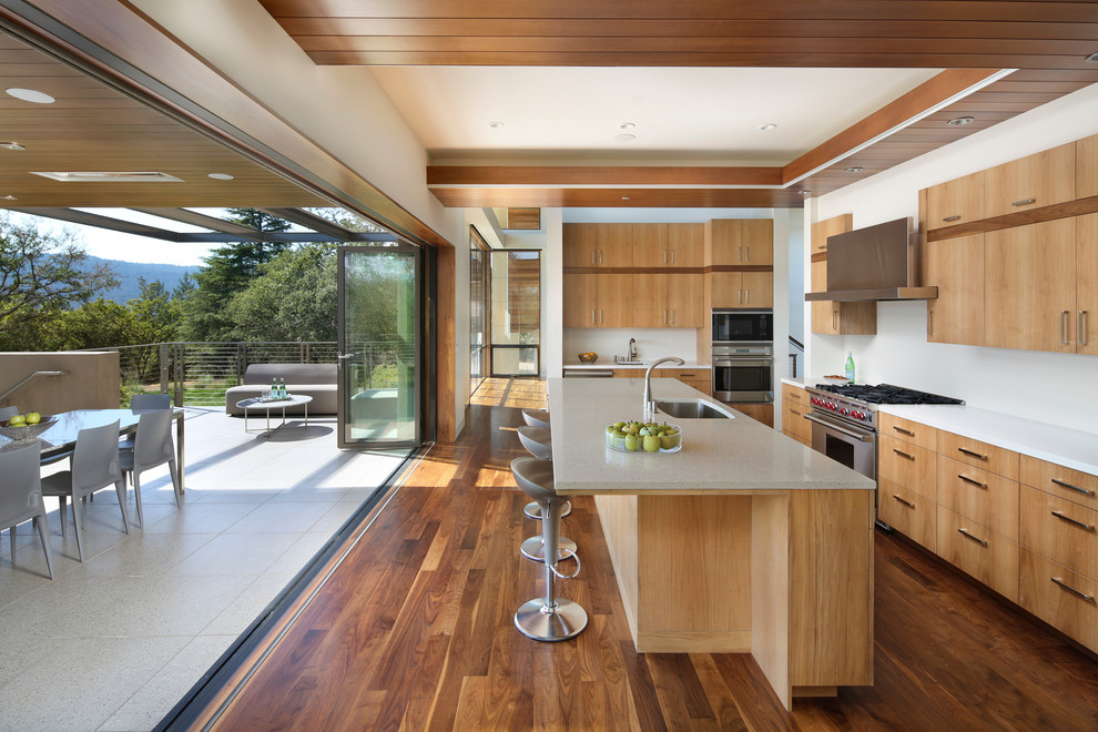 Moderne Wohnküche in L-Form mit Unterbauwaschbecken, flächenbündigen Schrankfronten, hellbraunen Holzschränken, Küchenrückwand in Weiß, Küchengeräten aus Edelstahl, dunklem Holzboden, Kücheninsel und braunem Boden in San Francisco
