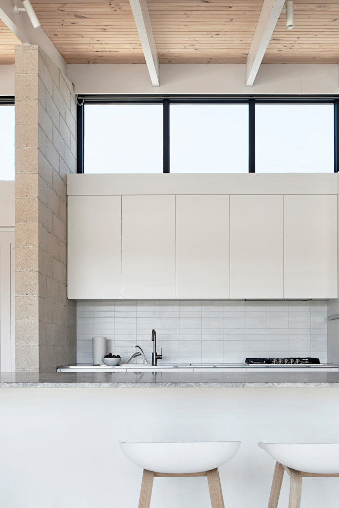 Zweizeilige Moderne Küche mit flächenbündigen Schrankfronten, weißen Schränken, Küchenrückwand in Gelb, Kücheninsel, grauer Arbeitsplatte, freigelegten Dachbalken und Holzdecke in Melbourne