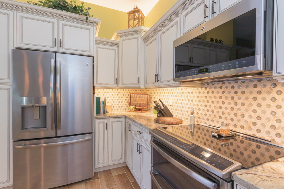 Example of a small classic u-shaped porcelain tile and brown floor enclosed kitchen design in Other with an undermount sink, raised-panel cabinets, white cabinets, granite countertops, multicolored backsplash, stone tile backsplash, stainless steel appliances and a peninsula