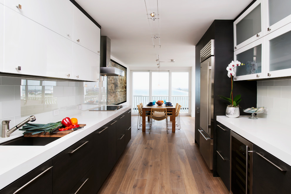 Bild på ett funkis kök, med släta luckor, svarta skåp, bänkskiva i kvarts, vitt stänkskydd, rostfria vitvaror, stänkskydd i tunnelbanekakel och mellanmörkt trägolv