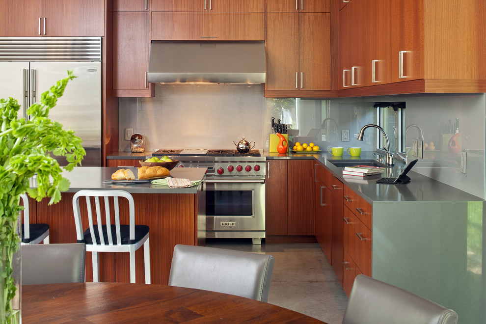 Modern inredning av ett mellanstort kök, med en undermonterad diskho, släta luckor, skåp i mellenmörkt trä, bänkskiva i kvarts, grått stänkskydd, glaspanel som stänkskydd, rostfria vitvaror, betonggolv och en köksö