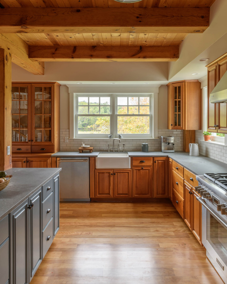 Bild på ett stort vintage grå grått l-kök, med luckor med upphöjd panel, skåp i mellenmörkt trä, vitt stänkskydd, stänkskydd i tunnelbanekakel, rostfria vitvaror, en köksö och brunt golv