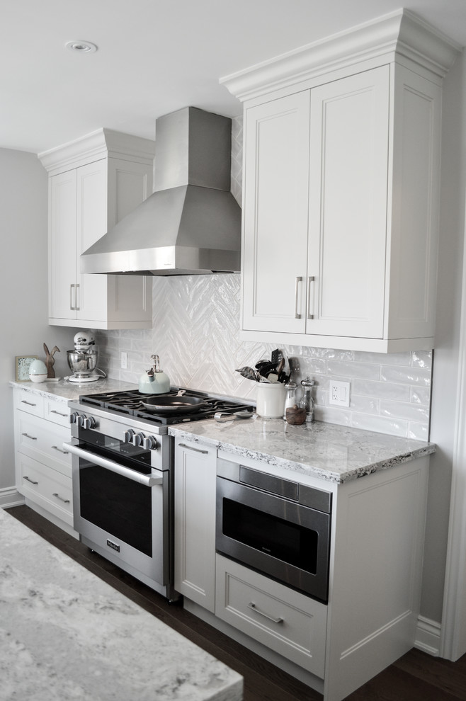 This is an example of a medium sized traditional l-shaped enclosed kitchen in Toronto with a submerged sink, shaker cabinets, engineered stone countertops, grey splashback, porcelain splashback, stainless steel appliances, medium hardwood flooring and an island.
