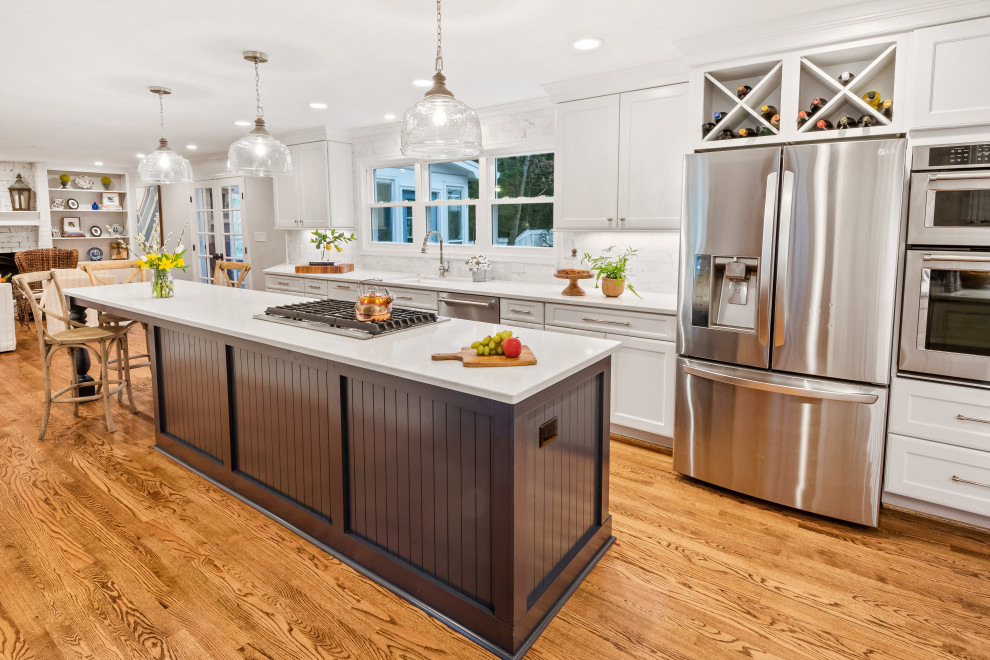This is an example of a medium sized coastal l-shaped kitchen/diner in Raleigh with shaker cabinets, white cabinets, engineered stone countertops, white splashback, marble splashback, stainless steel appliances, medium hardwood flooring, an island, brown floors and white worktops.