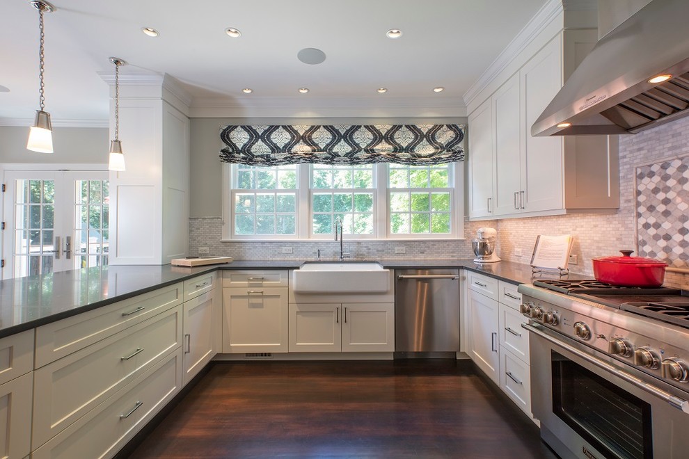 Example of a large transitional u-shaped dark wood floor and brown floor open concept kitchen design in DC Metro with a farmhouse sink, recessed-panel cabinets, white cabinets, quartz countertops, white backsplash, marble backsplash, stainless steel appliances, a peninsula and black countertops