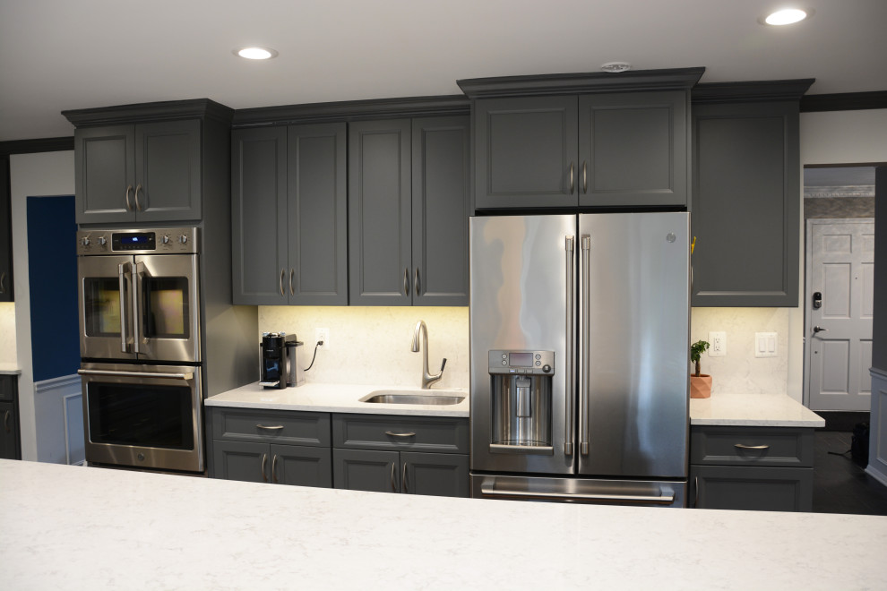 Inspiration for a large classic l-shaped enclosed kitchen in DC Metro with a single-bowl sink, recessed-panel cabinets, grey cabinets, engineered stone countertops, white splashback, engineered quartz splashback, stainless steel appliances, dark hardwood flooring, an island, brown floors and white worktops.