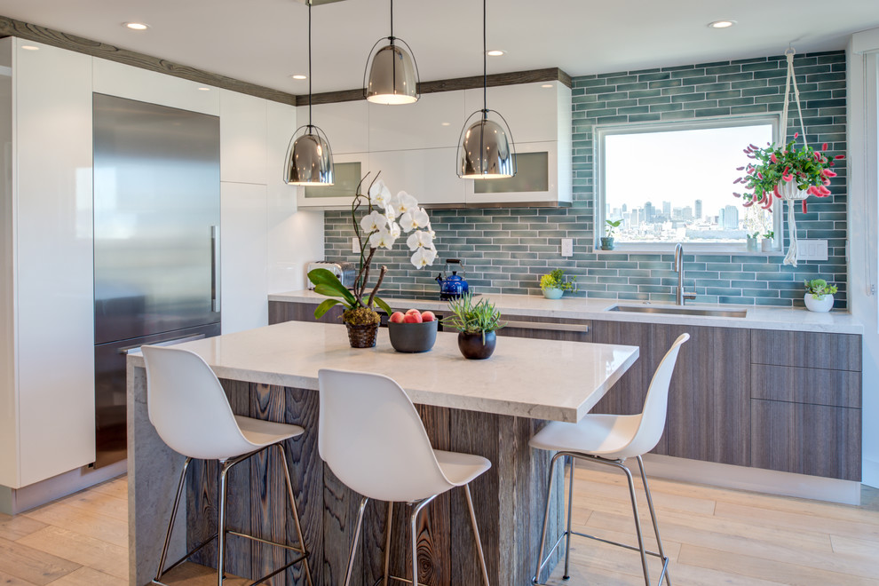 This is an example of a medium sized contemporary l-shaped kitchen in San Francisco with a submerged sink, flat-panel cabinets, white cabinets, composite countertops, green splashback, glass tiled splashback, light hardwood flooring, an island, beige floors and beige worktops.