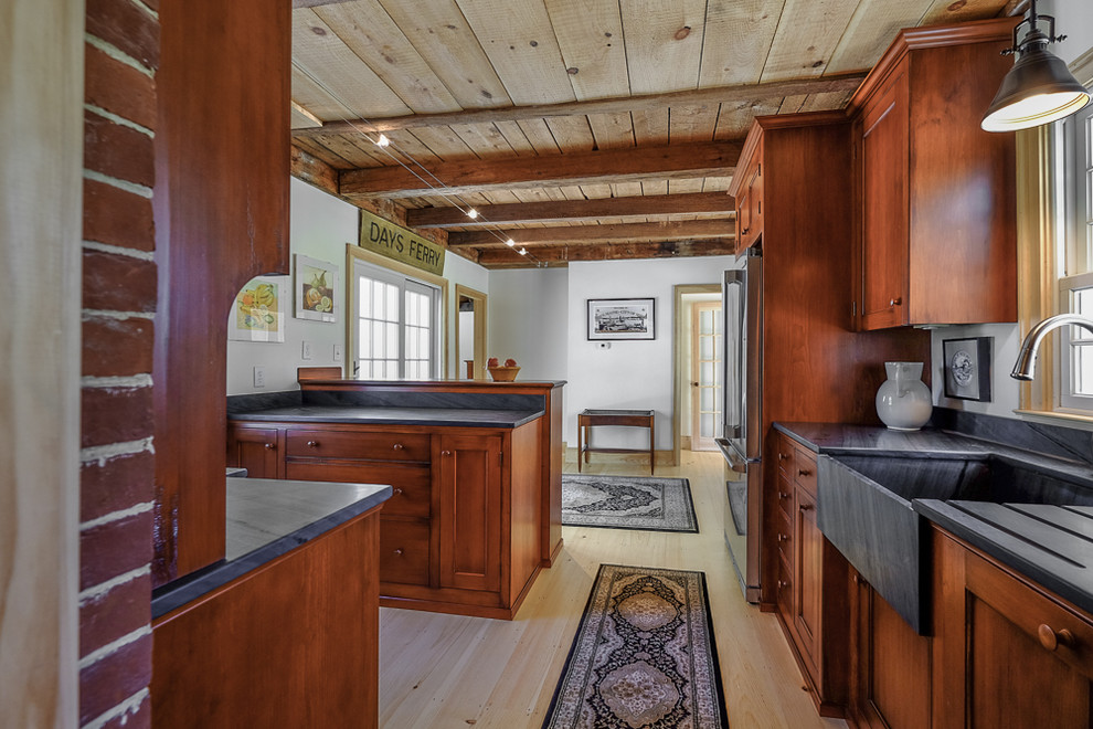 Small farmhouse l-shaped light wood floor enclosed kitchen photo in Portland Maine with a farmhouse sink, stainless steel appliances, a peninsula, recessed-panel cabinets, dark wood cabinets, soapstone countertops and red backsplash