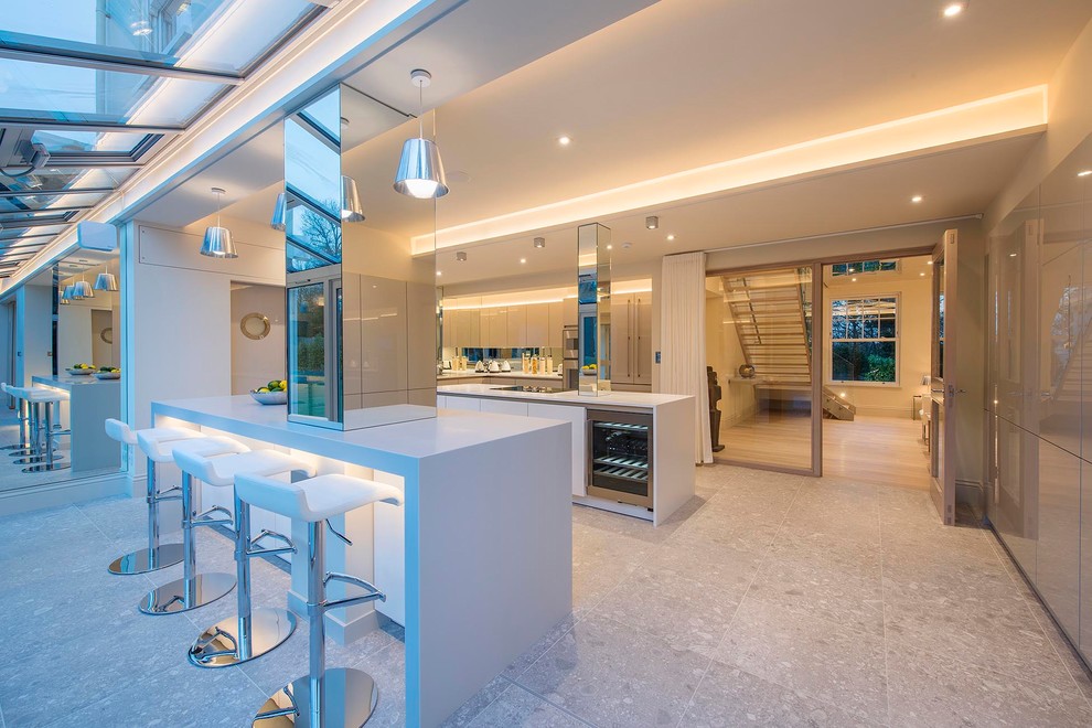 Photo of a large contemporary l-shaped open plan kitchen in Hertfordshire with an integrated sink, flat-panel cabinets, grey cabinets, composite countertops, metallic splashback, mirror splashback, stainless steel appliances, porcelain flooring, multiple islands, multi-coloured floors and white worktops.