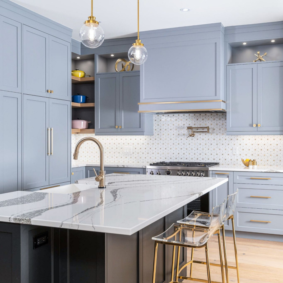 Inspiration for a classic l-shaped kitchen in Toronto with a belfast sink, shaker cabinets, blue cabinets, engineered stone countertops, light hardwood flooring, an island, white splashback, mosaic tiled splashback, stainless steel appliances, beige floors and white worktops.