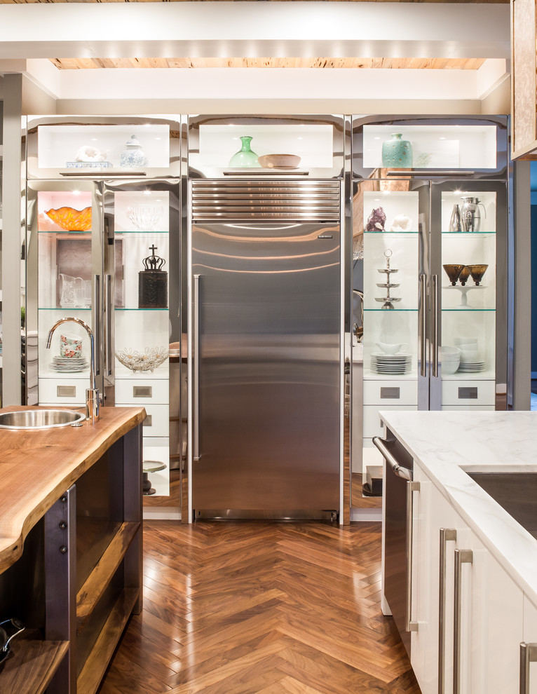 Aménagement d'une cuisine contemporaine en inox avec 2 îlots, un placard à porte vitrée, un sol en bois brun et un évier encastré.