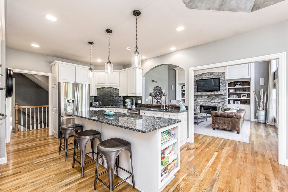 Example of a mid-sized mountain style u-shaped light wood floor eat-in kitchen design in Columbus with an undermount sink, raised-panel cabinets, white cabinets, granite countertops, black backsplash, porcelain backsplash, stainless steel appliances and an island