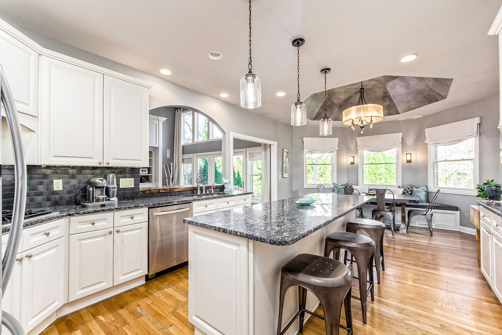 Inspiration for a mid-sized rustic u-shaped light wood floor eat-in kitchen remodel in Columbus with an undermount sink, raised-panel cabinets, white cabinets, granite countertops, black backsplash, porcelain backsplash, stainless steel appliances and an island