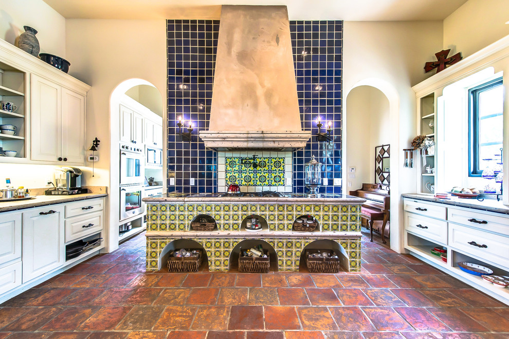 オースティンにある中くらいなサンタフェスタイルのおしゃれなキッチン (エプロンフロントシンク、ライムストーンカウンター、青いキッチンパネル、テラコッタタイルのキッチンパネル、テラコッタタイルの床、アイランドなし) の写真