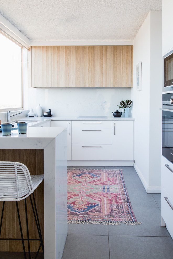 Cette photo montre une cuisine scandinave en U et bois clair avec un placard à porte plane, une crédence blanche, un électroménager en acier inoxydable et une péninsule.