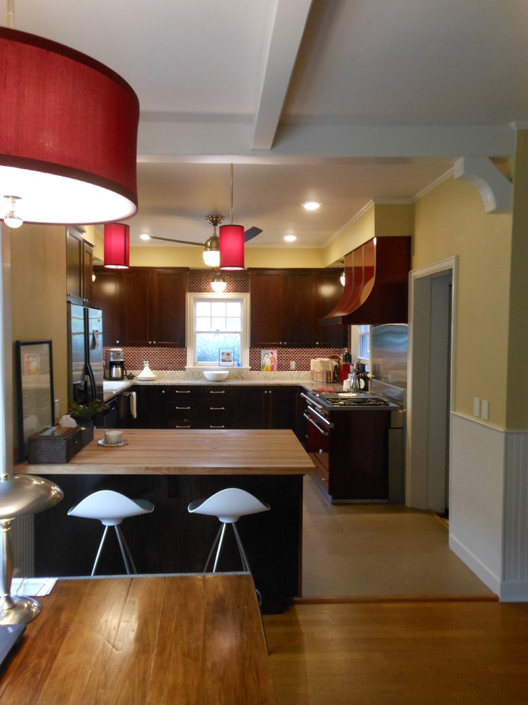 Klassisk inredning av ett mellanstort kök, med skåp i mörkt trä, granitbänkskiva, rött stänkskydd, stänkskydd i glaskakel, rostfria vitvaror, linoleumgolv och en halv köksö