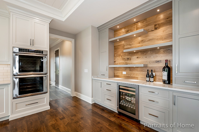 Photo of a large classic open plan kitchen in Chicago with a submerged sink, flat-panel cabinets, white cabinets, engineered stone countertops, white splashback, metro tiled splashback, stainless steel appliances, medium hardwood flooring, an island and brown floors.