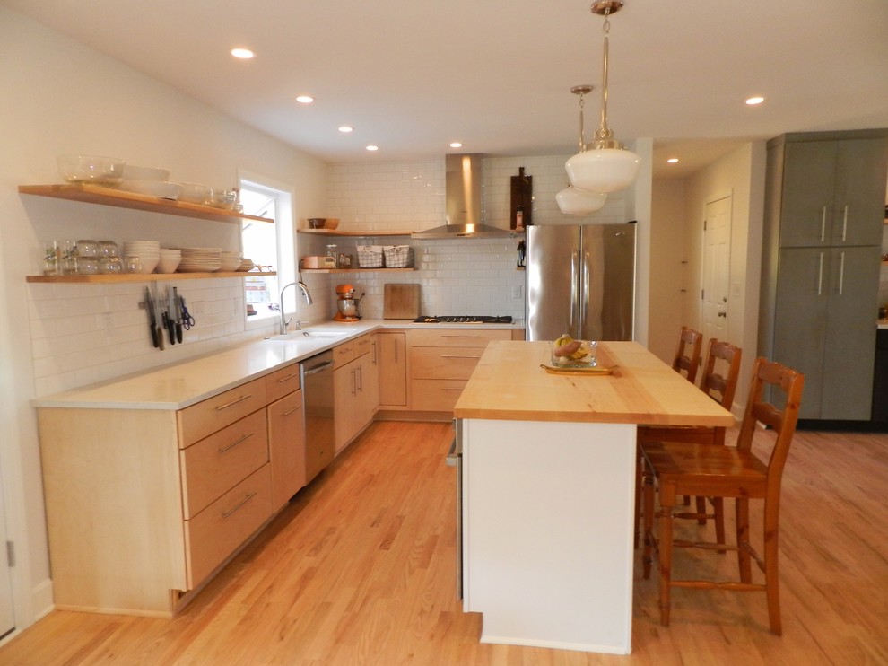 Foto på ett lantligt kök, med en undermonterad diskho, släta luckor, skåp i ljust trä, marmorbänkskiva, vitt stänkskydd, stänkskydd i tunnelbanekakel, rostfria vitvaror, ljust trägolv och en köksö