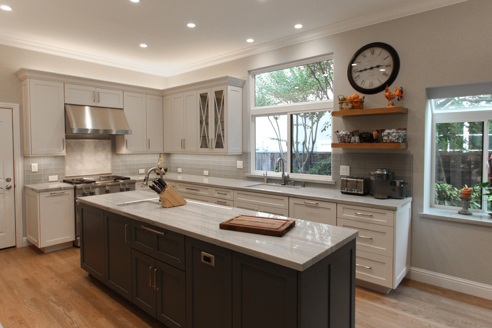 Design ideas for a medium sized classic u-shaped open plan kitchen in San Francisco with a submerged sink, shaker cabinets, white cabinets, quartz worktops, grey splashback, glass tiled splashback, stainless steel appliances, light hardwood flooring, an island, brown floors and grey worktops.