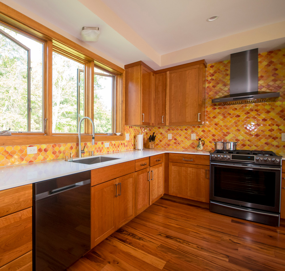 Foto på ett stort funkis kök, med en enkel diskho, skåp i shakerstil, skåp i mellenmörkt trä, bänkskiva i kvartsit, orange stänkskydd, stänkskydd i mosaik, svarta vitvaror, mellanmörkt trägolv och en köksö