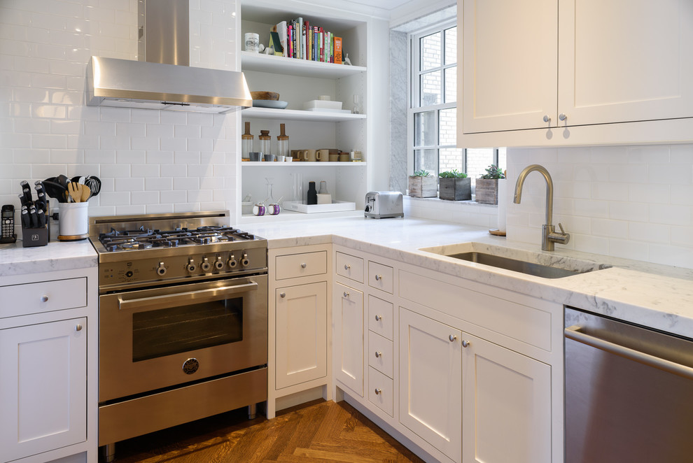 Foto på ett mellanstort vintage kök, med en undermonterad diskho, luckor med infälld panel, vita skåp, marmorbänkskiva, vitt stänkskydd, stänkskydd i keramik, rostfria vitvaror, mellanmörkt trägolv och brunt golv