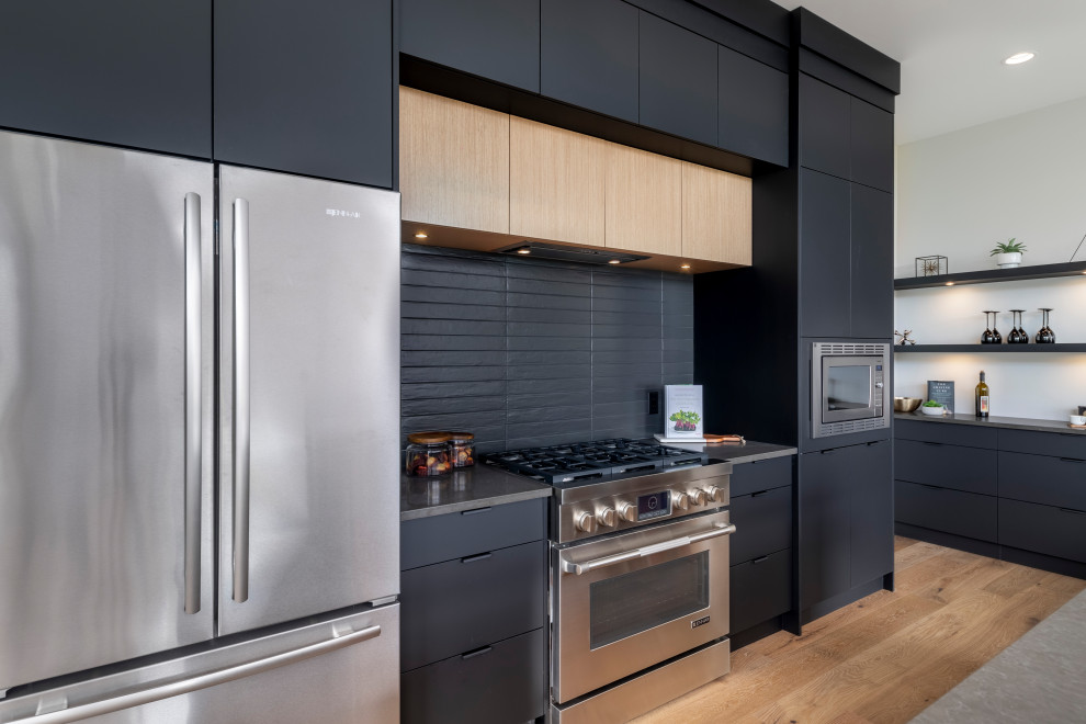 Design ideas for a medium sized contemporary l-shaped kitchen/diner in Vancouver with a submerged sink, flat-panel cabinets, black cabinets, black splashback, stainless steel appliances, medium hardwood flooring, an island, brown floors and grey worktops.