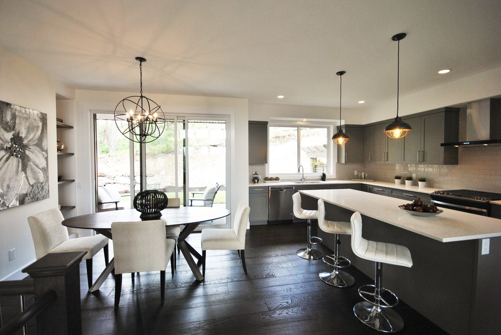 Photo of a small contemporary grey and cream l-shaped kitchen/diner in Vancouver with a submerged sink, shaker cabinets, grey cabinets, engineered stone countertops, white splashback, metro tiled splashback, stainless steel appliances, dark hardwood flooring, an island and brown floors.