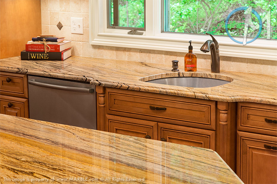 Cette photo montre une grande cuisine américaine tendance en L et bois clair avec un évier encastré, un plan de travail en granite, une crédence beige, un électroménager en acier inoxydable, un sol en bois brun et îlot.
