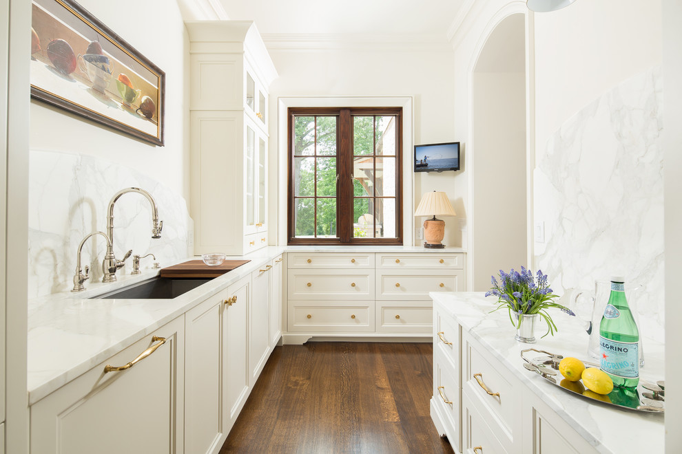 Klassisk inredning av ett mycket stort kök, med en undermonterad diskho, luckor med infälld panel, vita skåp, marmorbänkskiva, grått stänkskydd, stänkskydd i marmor, rostfria vitvaror, mellanmörkt trägolv och en köksö