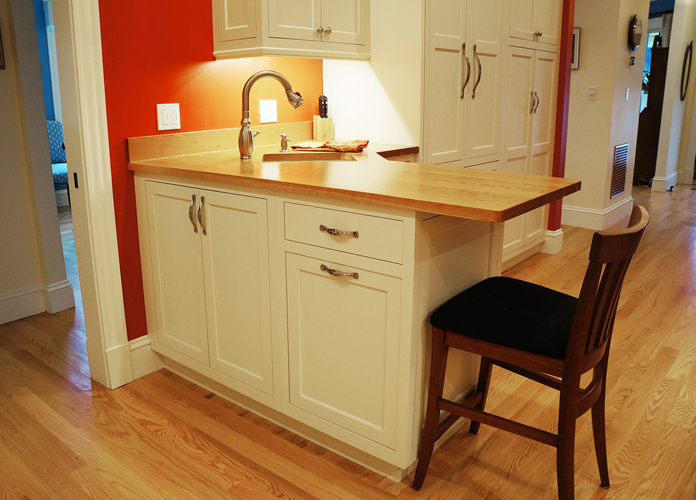 Foto på ett mellanstort vintage kök, med en undermonterad diskho, luckor med infälld panel, vita skåp, träbänkskiva, stänkskydd i mosaik, integrerade vitvaror, mellanmörkt trägolv och en halv köksö