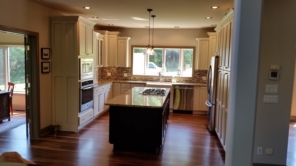 Exempel på ett avskilt, litet klassiskt u-kök, med en rustik diskho, rostfria vitvaror, en köksö, luckor med infälld panel, beige skåp, granitbänkskiva, flerfärgad stänkskydd, stänkskydd i glaskakel, målat trägolv och brunt golv