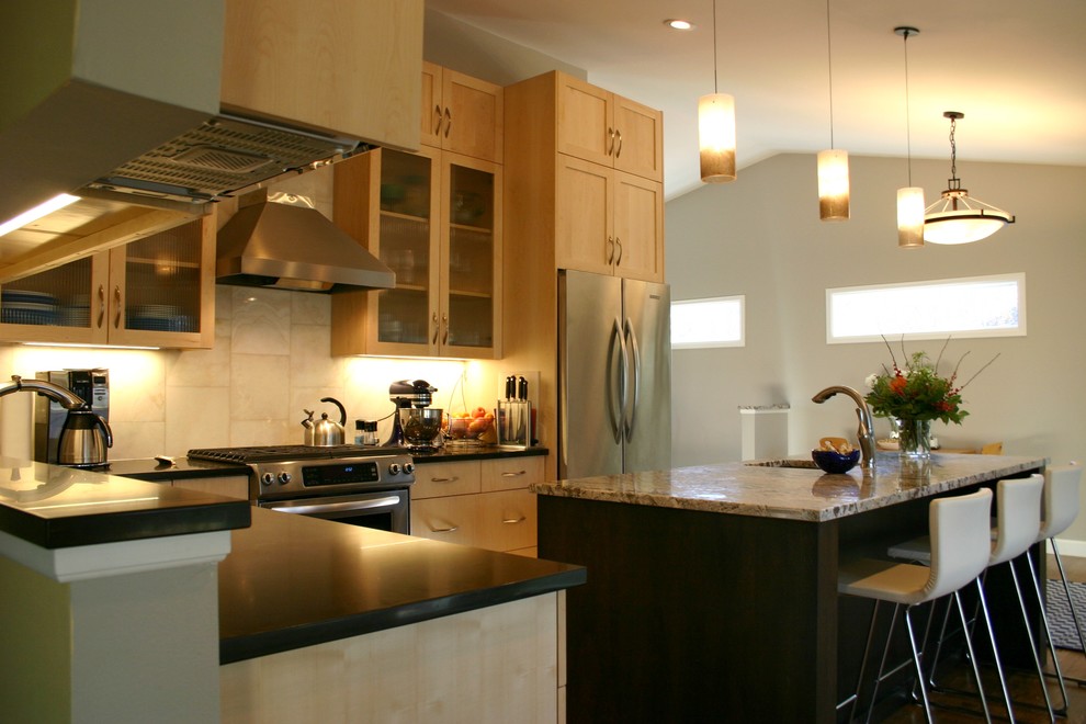 Bild på ett mellanstort funkis kök, med en undermonterad diskho, skåp i ljust trä, granitbänkskiva, beige stänkskydd, rostfria vitvaror, mellanmörkt trägolv och en köksö
