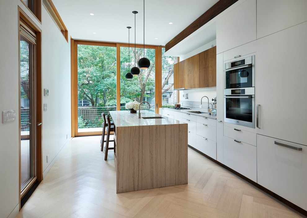 This is an example of a medium sized contemporary u-shaped kitchen/diner in New York with a submerged sink, flat-panel cabinets, white cabinets, marble worktops, grey splashback, marble splashback, stainless steel appliances, light hardwood flooring, an island, beige floors and beige worktops.