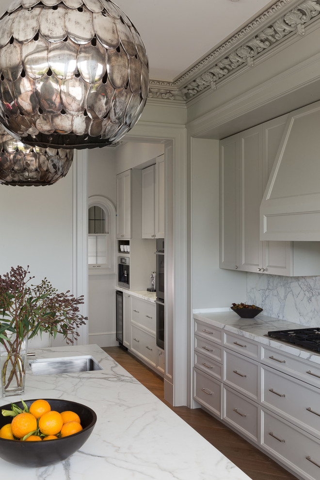 Idée de décoration pour une cuisine ouverte parallèle tradition avec un placard à porte shaker, des portes de placard grises, une crédence blanche, une crédence en dalle de pierre, un sol en bois brun et îlot.