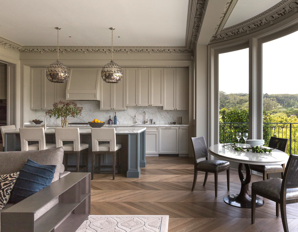 Example of a transitional galley medium tone wood floor open concept kitchen design in San Francisco with shaker cabinets, gray cabinets, white backsplash, stone slab backsplash and an island