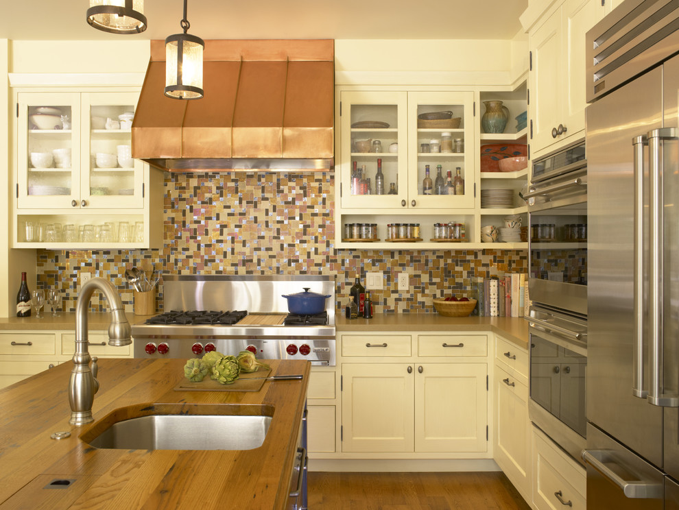 サンフランシスコにあるトラディショナルスタイルのおしゃれなキッチン (モザイクタイルのキッチンパネル、シルバーの調理設備、木材カウンター、マルチカラーのキッチンパネル、ガラス扉のキャビネット、白いキャビネット、アンダーカウンターシンク、無垢フローリング、茶色い床、茶色いキッチンカウンター) の写真