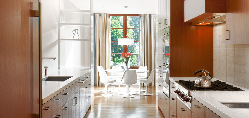 Example of a mid-sized minimalist galley light wood floor and brown floor eat-in kitchen design in San Francisco with flat-panel cabinets, medium tone wood cabinets, white backsplash, glass tile backsplash, an undermount sink, stainless steel appliances and no island