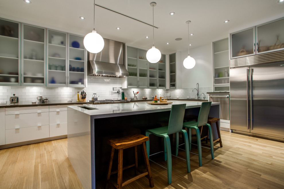 Example of a huge trendy u-shaped light wood floor open concept kitchen design in Dallas with an undermount sink, glass-front cabinets, white cabinets, solid surface countertops, white backsplash, glass tile backsplash, stainless steel appliances, an island and multicolored countertops