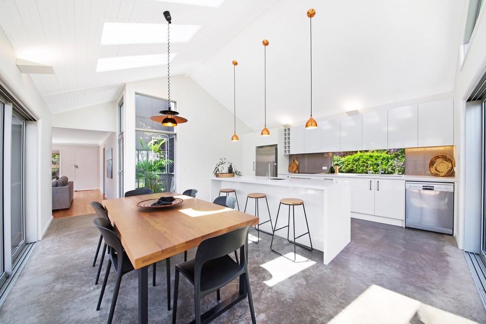 Modern inredning av ett mellanstort kök, med en undermonterad diskho, vita skåp, bänkskiva i kvarts, beige stänkskydd, glaspanel som stänkskydd, rostfria vitvaror, betonggolv, en köksö och grått golv
