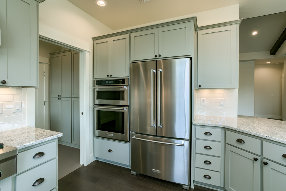 Example of a mid-sized arts and crafts l-shaped dark wood floor and brown floor open concept kitchen design in Portland with a farmhouse sink, shaker cabinets, gray cabinets, granite countertops, white backsplash, subway tile backsplash, stainless steel appliances and an island